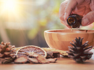 Dark glass bottle with essential oil blend with cinnamon, dried citrus slice, pine twigs, cones and...