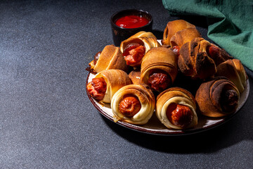 Traditional Christmas dish recipe Pigs in blankets, sausages wrapped in bacon, oven baked puff pastry hot dogs rolls with xmas tree branches, decoration and gifts on black table 