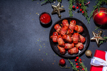 Traditional Christmas dish recipe Pigs in blankets, sausages wrapped in bacon, oven baked puff pastry hot dogs rolls with xmas tree branches, decoration and gifts on black table 