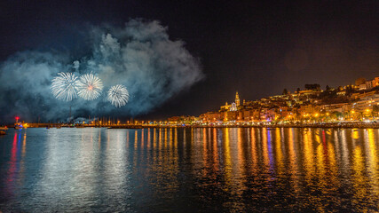 Feu d'artifice du 15 août pour les fêtes de l'assomption à Menton avec les reflets des lumières de la ville sur la mer