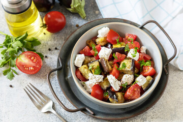 Healthy vegetarian diet food. Salad with grill eggplants, tomatoes and feta cheese on a gray stone tabletop.