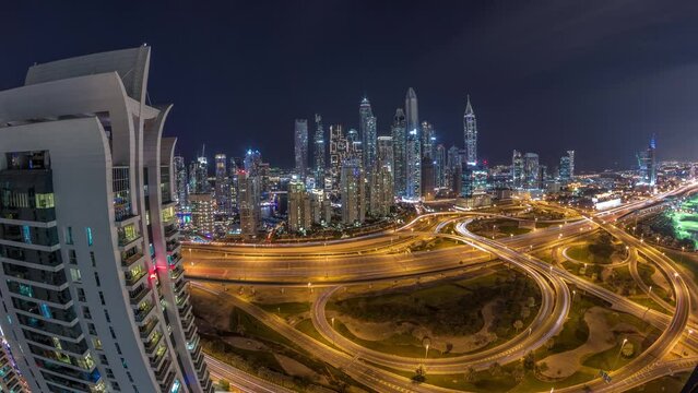 Panorama of Dubai Marina after sunset highway intersection spaghetti junction day to night transition timelapse. Illuminated tallest skyscrapers on a background. Aerial top view from JLT district.