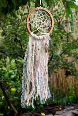 Dream catcher crocheted from threads on a wooden base, decorated with lace, threads, feathers and wooden beads outdoors