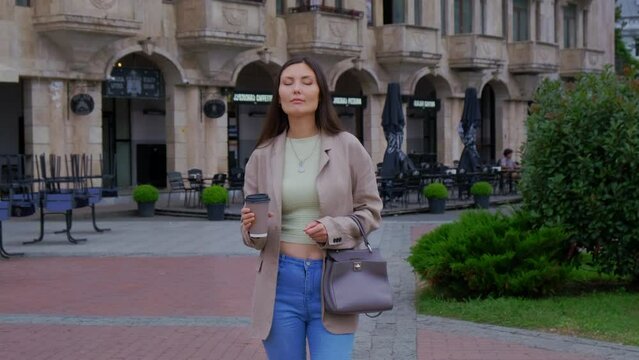 Unhappy Woman Drink Coffee at the Morning on the Street. Disgruntled Female Stands on the Square in the City.