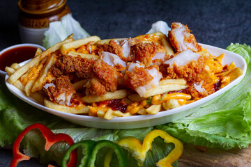 Dish of cheesy fish popcorn fries at cafe restaurant. American fast food dish, consisting of french fries covered in cheese.