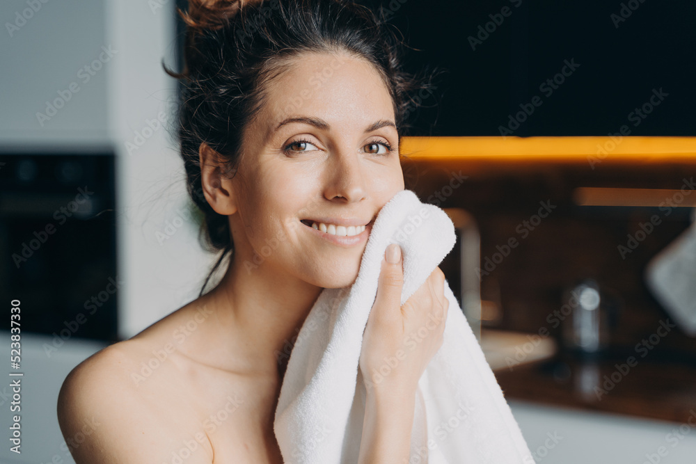 Wall mural european girl is wiping face with towel after washing. young brunette woman takes shower at home.