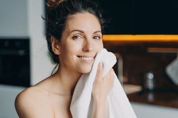 European girl is wiping face with towel after washing. Young brunette woman takes shower at home.