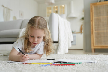Talented preschool kid girl painting with colored pencils, lying on floor at home. Child creativity