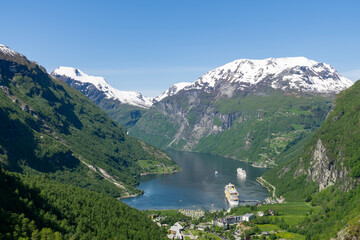 Fototapeta na wymiar Geiranger Fjord and village Geiranger surrounded by high green and snowy mountains in Norway.