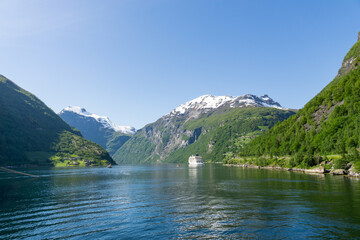 Fototapeta na wymiar Geiranger Fjord surrounded by high green, snow-capped mountains and a ship.