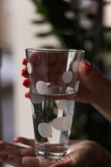 Closeup of glass of water in woman's hands. Arms with pink manicure holding spotted glass with water. Healthy lifestyle. Green grass in background.