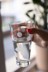 Closeup of glass of water in woman's hands. Arms with pink manicure holding spotted glass with water. Healthy lifestyle. Green grass in background.