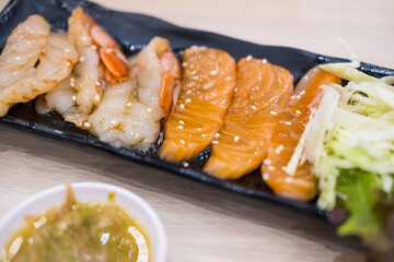 Raw salmon with raw shrimp, pickled in Korean sauce, on a black tray