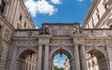 London, UK - July 4, 2022: Along Parliament street A3212, Beige stone Triple-Arched bridge top across King Charles Street with focus on central frieze and statues under blue cloudscape
