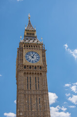 Fototapeta na wymiar London, UK - July 4, 2022: Big Ben tower top half against blue cloudscape shows golden trim, clock and spire.