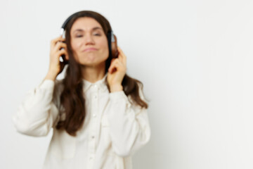Fototapeta premium portrait of a beautiful happy woman with long dark hair happily listening to music with headphones on a light monochrome background for inserting an advertising layout
