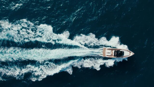 Top view slow motion drone shot of luxury motorboat in ocean waters near marina. Panning shot of yacht swim and raise waves in open blue waters. Amazing epic background over waves in sea