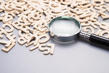Magnifying glass on the pile of wooden English alphabets, glossary, and keyword, search the right...