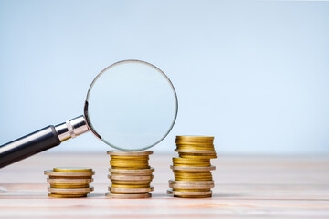 Magnifying glass on a few stacks of money coins that gradually increase, check the financial status, budget, and savings, sales increase a little at a time
