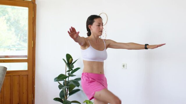A young woman is doing exercises for good health and body strengthening. Raises arms and legs directly in front of the laptop. The girl is doing yoga at home.