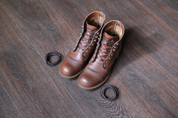 pair of brown leather shoes are prepared for cleaning and brushing and  laces lies on wooden floor