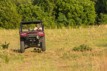Senior man driving UTV 4 X 4 fast over a hill in a field 