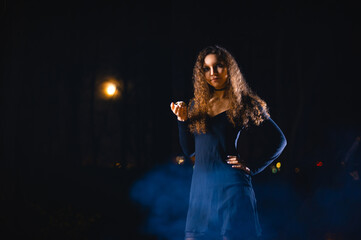 White curly girl in the image of a witch in the moonlight on a Halloween holiday. The witch is holding a small skull in her hands