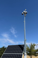 A CCTV mobile camera tower with a solar panel in a shopping center parking lot.