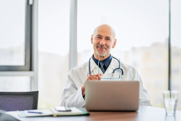 Male doctor using cellphone and laptop while working in doctor's room