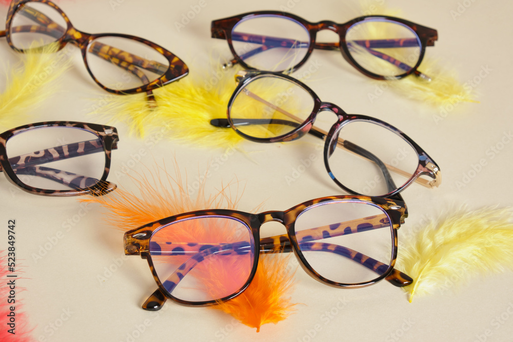 Poster eyeglasses on beige background with colored feathers