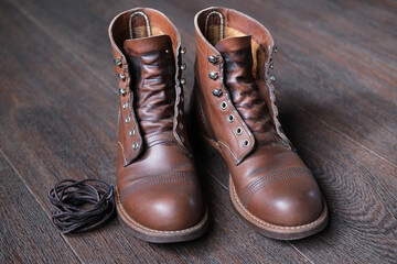 leather work boots without laces next to shoelaces on wooden floor, shoes are prepared to care and cleaning