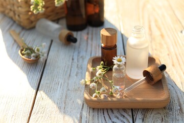Fototapeta na wymiar Chamomile essential oil, pipette and flowers on white wooden table outdoors, space for text