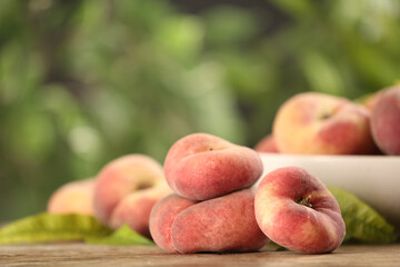 Fresh ripe donut peaches on wooden table against blurred green background. Space for text