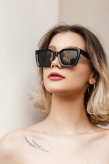Naklejka premium Beautiful female headshot portrait of a pretty stylish young girl with a nose piercing with black fashion sunglasses on a white background on the street