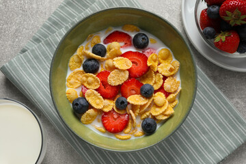 Corn flakes with berries in bowl served on grey table, flat lay