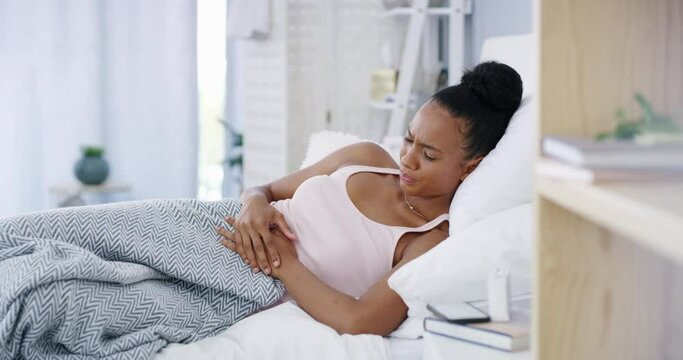 Woman sick with stomach cramps in bed from period pain or illness. Young female feeling unhappy at home because of sore abdomen. Lady upset that she will have to stay inside due to tummy issues.
