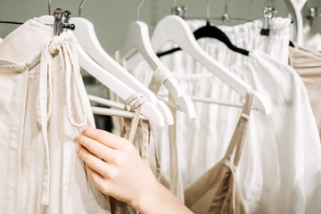 Sustainable fashion, slow fashion. Close Up Shot of female hand taking clothing rack with natural tones clothes