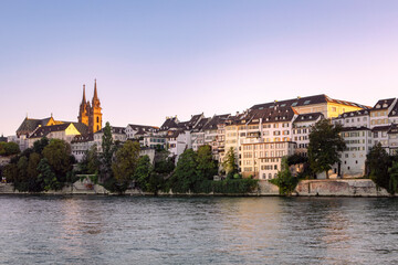 Cityscape of Basel in Switzerland by Rhine river. View on the old town architecture and Basel Minster. Buildings on the river bank by evening light.