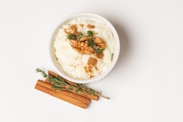 Top view of creamy rice pudding with walnuts, cinnamon sticks and thyme stems in a white form on...