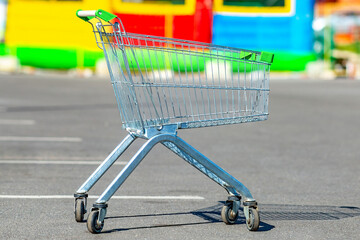 Empty shopping cart in selective focus in the parking lot of a shop or mall, supermarket. Food basket. Grocery сrisis сoncept.