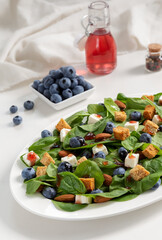 Blueberry, almond and goat cheese spinach salad with homemade croutons and berry dressing on white plate. Vertical.