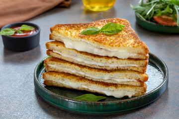 Sliced fried sandwich with melted mozzarella on a plate served with tomato dipping sauce and arugula salad. Italian grilled cheese sandwich Mozzarella in carrozza. - obrazy, fototapety, plakaty