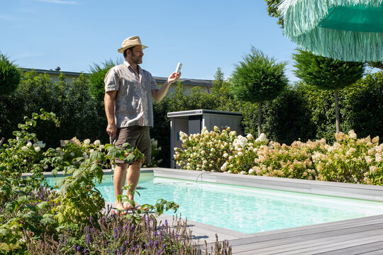Mann mit Strohhut, im Sommer, pr&uuml;ft denn Chlorgehalt und den PH Wert des Pools mit Hilfe eines Teststreifens.