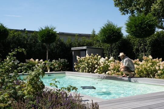 Mann mit Strohhut reinigt den Pool im Sommer und kontrolliert Poolroboter.