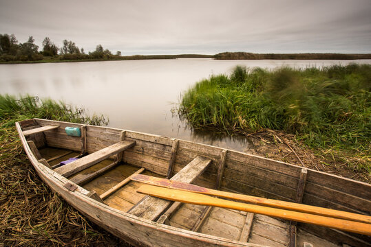 An old wooden boat on the river bank in a remote European location. Vintage style photo.