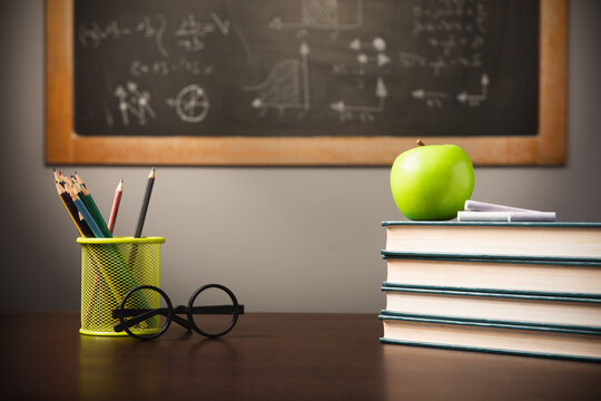 Back to school background with books, pencils and apple over chalkboard and wooden table