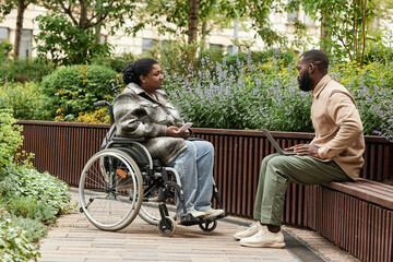 Side view portrait of black woman in wheelchair talking to friend or partner in city garden