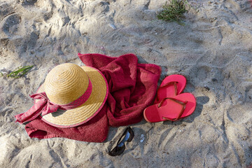 Summer beach vacations, straw hat and flip flops on a red towel in the sand near the tourist resort Boltenhagen, Baltic Sea, Germany, copy space, view from above