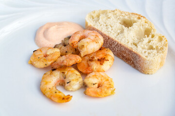 Roasted shrimps or prawns with cocktail sauce and bread on a white plate as appetizer at a dinner copy space, selected focus