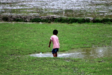 A young boy or children or teenage is playing in the muddy field alone.Green background.